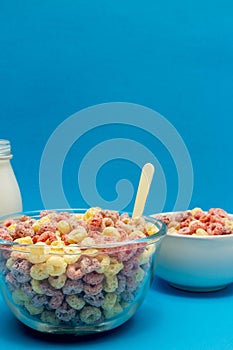 Healthy breakfast concept, Colorful ring cereals in glass bowl and milk on light blue background