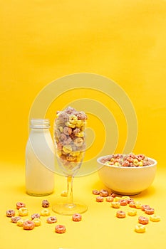 Healthy breakfast concept, Colorful ring cereals in glass and bowl with milk on yellow background
