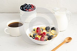 Healthy breakfast with cornflakes in a white plate, berries, milk and coffee on a white background