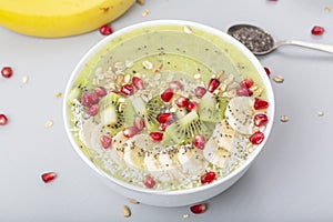 Healthy breakfast detox green smoothie with banana, kiwi, spinach, chia and pomegranate seed in a Bowl.