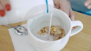 Healthy breakfast. Female hands pouring milk or yogurt into a bowl of cereal.