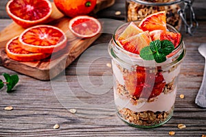 Healthy breakfast glass jar yoghurt parfait with homemade granola and blood orange on a wooden background