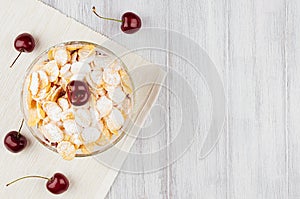 Healthy breakfast with golden corn flakes, ripe cherries, powdered sugar on white wood board top view, copy space.