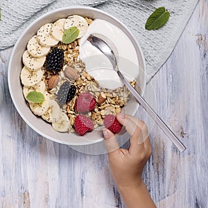 Healthy breakfast with granola, berries and yogurt, child`s hand holding rasbberry