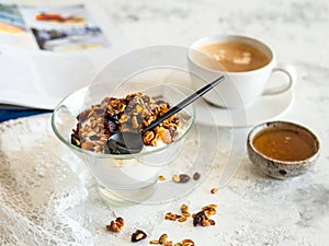 Healthy breakfast. Granola, muesli with pumpkin seeds, honey, yogurt in a glass bowl with a cup of coffee on white