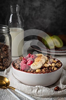 Healthy breakfast granola in a plate with nuts, banana and raspberries