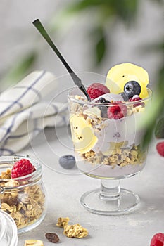 Healthy breakfast. Granola with raspberries, blueberries and golden kiwi. Glass of muesli, berries and yogurt parfait on the table