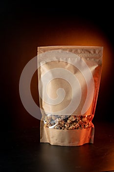 A healthy breakfast granola of various cereals in a yellow kraft paper bag. On a black background with orange light. Vertical