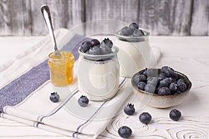 A healthy breakfast of Greek yogurt in a glass jar and fresh blueberries and jam at a rustic white table. Selective