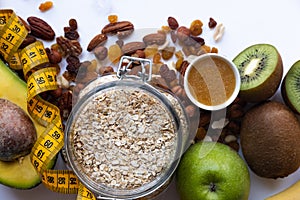 Healthy breakfast ingrediens. Homemade granola in open glass jar, honey, nuts, fruits, yellow tape-lane on white background.