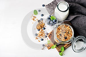 Healthy breakfast ingrediens. Homemade granola in open glass jar, milk or yogurt bottle, blueberries and mint