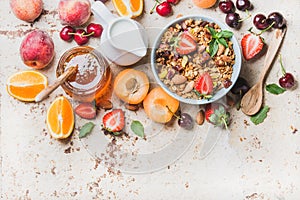 Healthy breakfast ingredients. Oat granola in bowl with nuts, strawberry and mint leaves, milk in pitcher, honey in