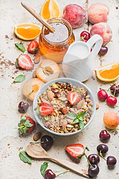 Healthy breakfast ingredients. Oat granola in bowl with nuts, strawberry and mint, milk in pitcher, honey in glass jar