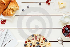 Healthy breakfast with oat flakes, berries, croissants on the white wooden table with copy space, top view