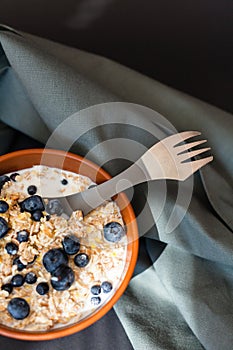 Healthy breakfast. Oat granola with fresh blueberries, currants and milk in a clay bowl over dark grunge surface. Top view