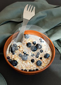 Healthy breakfast. Oat granola with fresh blueberries, currants and milk in a clay bowl over dark grunge surface. Top view