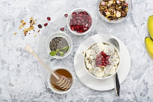 Healthy breakfast oatmeal with pomegranate, bananas, seeds and nuts, overhead scene on white marble. Top view