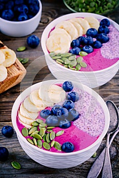 Healthy breakfast: purple smoothie bowl with chia pudding, banana, fresh blueberries and pumpkin seeds