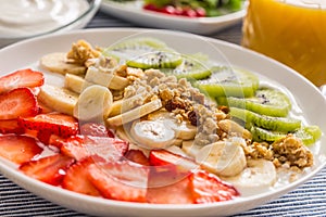 Healthy breakfast served with plate of yogurt muesli kiwi strawberries and banana