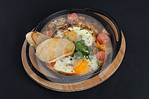 Healthy breakfast shakshuka - fried eggs, onion, bell pepper, tomatoes and spices in cast iron stewpan on old wooden plank