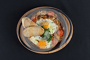 Healthy breakfast shakshuka - fried eggs, onion, bell pepper, tomatoes and spices in cast iron stewpan on old wooden plank