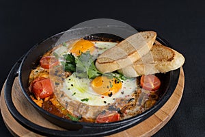 Healthy breakfast shakshuka - fried eggs, onion, bell pepper, tomatoes and spices in cast iron stewpan on old wooden plank