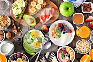 Healthy breakfast table scene with fruit, yogurts, smoothie bowl, oatmeal, nutritious toasts and egg skillet, above view over wood
