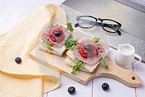 Healthy breakfast with toasted bread, milk, ham, vegetables, strawberry, jam and blueberry topping on wooden plate. Top view with