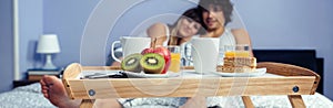 Healthy breakfast on tray and couple lying in background