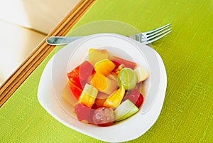 Healthy breakfast various fresh organic fruits salad in a white Bowl with fork under morning light on green table background, top