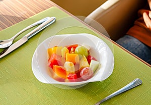 Healthy breakfast various fresh organic fruits salad in a white Bowl with fork under morning light on green table background, top