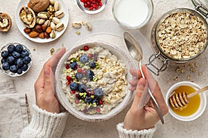 Healthy breakfast. Woman eating oatmeal porridge with fresh berry, nuts and honey photo