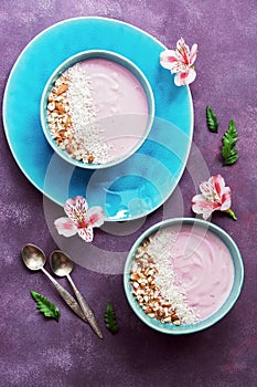 Healthy Breakfast-yogurt with almonds and coconut flakes in a blue bowl on a purple background decorated with flowers of