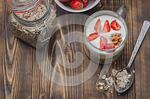 Healthy breakfast. Yogurt, fresh strawberry,  spoon with the scattered granule on a wooden table. Copyspace, top view