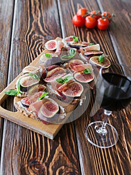 Healthy bruschettas with bread, cream cheese, prosciutto, figs and basil on rustic wooden table