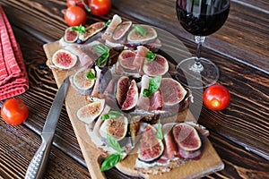 Healthy bruschettas with bread, cream cheese, prosciutto, figs and basil on rustic wooden table