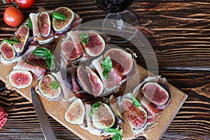 Healthy bruschettas with bread, cream cheese, prosciutto, figs and basil on rustic wooden table