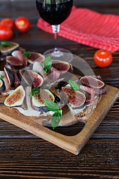 Healthy bruschettas with bread, cream cheese, prosciutto, figs and basil on rustic wooden table