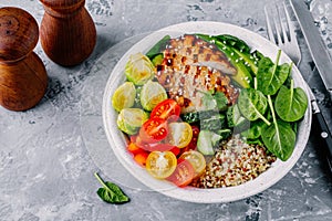 Healthy buddha bowl lunch with grilled chicken, quinoa, spinach, avocado, brussels sprouts, tomatoes, cucumbers on dark grey back