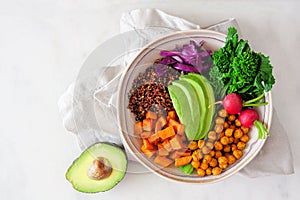 Healthy Buddha bowl with rapini, quinoa, sweet potato, chickpeas and avocado, above view over white marble photo