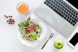 Healthy business lunch in the office, view of dish on white wooden desk near tablet and open organizer. Salad plate with salmon.