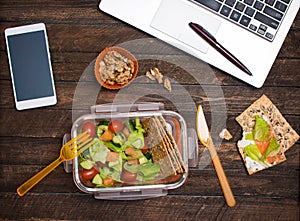 Healthy business lunch at workplace. Salad, salmon, avocado and bread crisps lunch box on working desk with laptop, smartphone