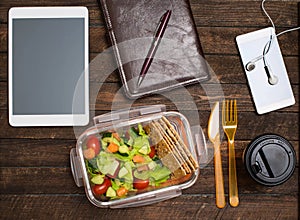 Healthy business lunch at workplace. Salad, salmon, avocado and nuts lunch box on working desk with tablet computer, smartphone,