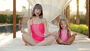 Healthy caucasian mother teaching meditation sitting with cute small child daughter