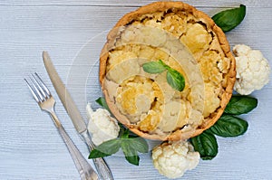 Healthy cauliflower pie decorated with fresh basil leaves and vintage silver knife and fork. Vegetarian cauliflower tart