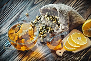 Healthy chamomile tea cup, hessian bag of dry daisies flowers, honey jar and lemon slices