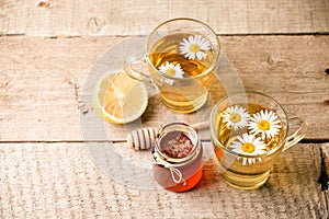 Healthy chamomile tea poured into glass cup. Teapot, small honey jar, heather bunch and glass jar of daisy medicinal herbs