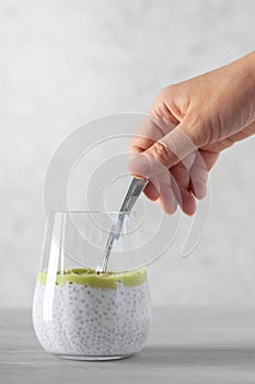 Healthy chia pudding made with avocado and seeds, hand with spoon. White background.