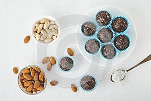 Healthy chocolate energy bites with nuts, dates, cocoa powder, coconut flakes on white table.