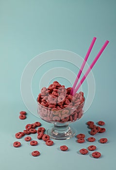 healthy corn flakes for breakfast in the form of pink rings in a transparent glass on a bright yellow background